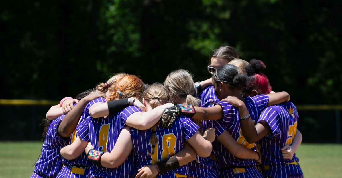A unified softball team of young women in a huddle on a sunny day, showcasing teamwork and sportsmanship.